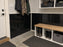 Mudroom entry with black HDPE wall liner installed behind a boot bench and coat hooks
