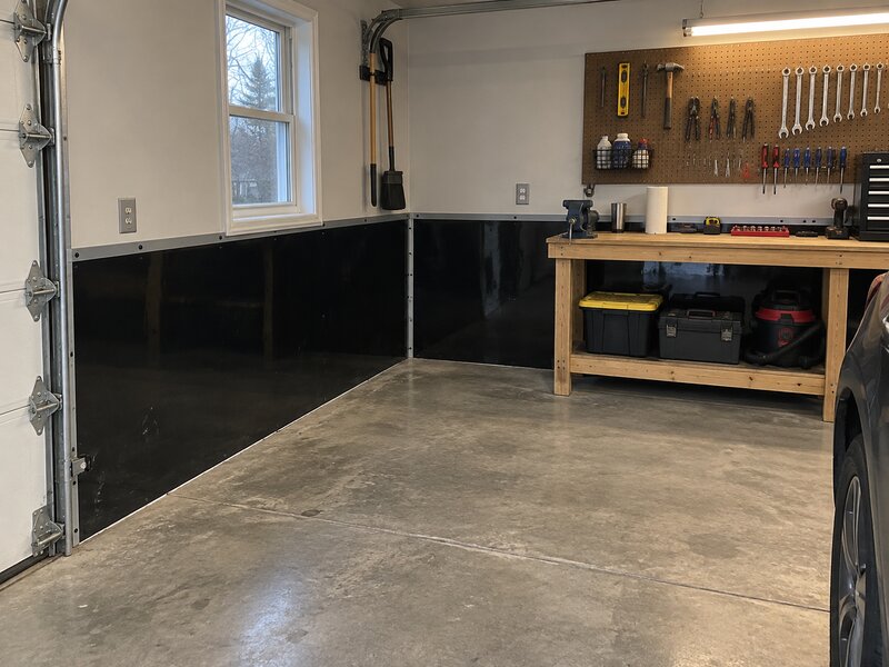 Garage with black HDPE wall liner installed along the lower walls beside a workbench and pegboard
