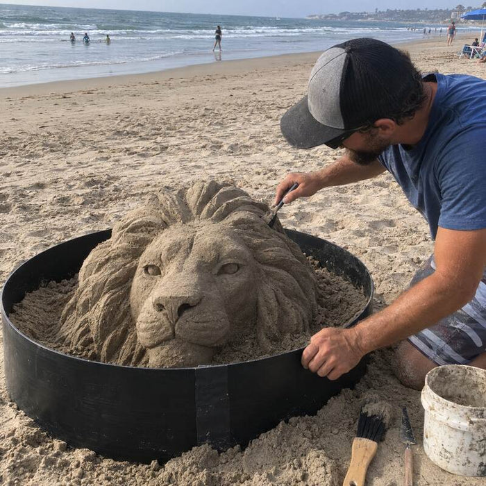 Sand sculptor using an HDPE plastic form ring to carve a lion head sand sculpture on the beach
